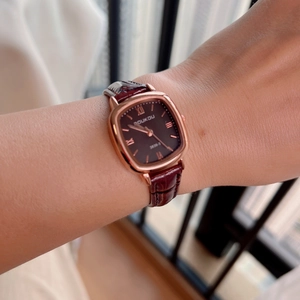 Close-up of elegant square rose gold watch with burgundy leather strap worn on wrist