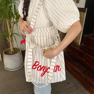 Detail of striped canvas tote bag with red Bonjour embroidery worn by a model