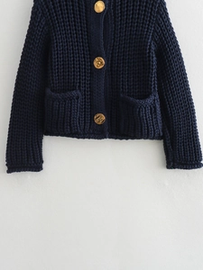 Detail of dark blue chunky knit cardigan featuring textured gold buttons and front pockets