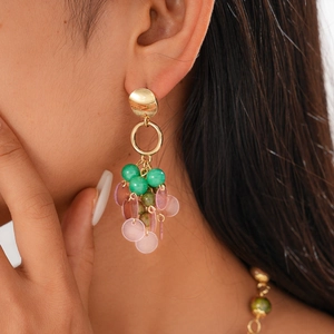 Detailed view of bohemian gold drop earrings with emerald green beads and purple discs