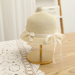 Detail of straw hat with white lace trim and bows on an elegant gold display stand