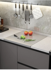 Large stainless steel cutting board on kitchen counter with fresh vegetables and knife