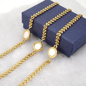 Detail showing leaf-shaped woven gold chain and round shell pendant on dark blue box