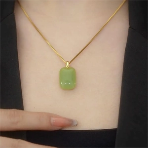 Elegant gold necklace with emerald green rectangular pendant worn on a black blazer
