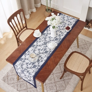 Linen table runner with blue floral patterns and elegant lace edges on a wooden table