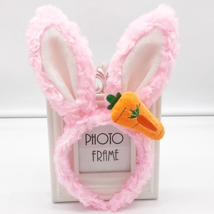 Plush pink bunny ears headband with cute carrot accessory shown on a white frame stand