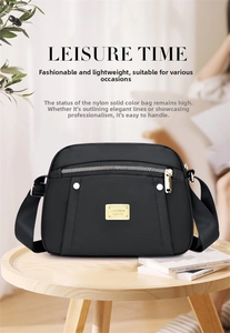 Detail view of a black nylon crossbody bag with gold metal logo and zipper compartments