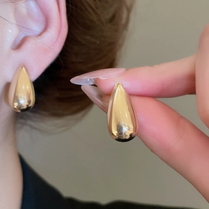 Detailed view of smooth gold-tone teardrop earrings held by hand and worn by a model