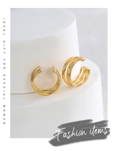 Macro detail of gold-plated triple-line ear cuffs on minimalist white geometric steps
