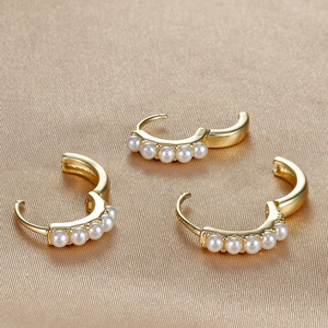 Macro shot of three 18K gold-plated pearl hoop earrings on elegant silk fabric background