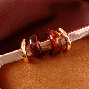 Close-up of geometric C-shaped earrings in polished 18K gold and amber resin texture