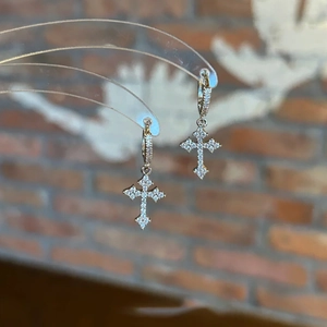 Detailed view of glittering cross pendant earrings with zircon stones on a display stand