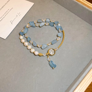 Dettaglio del bracciale a doppio strato con pietre blu, perle e ciondolo dorato