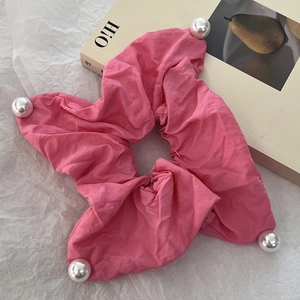 Detail of pink fabric scrunchie with soft pleats and white pearl beads on white paper