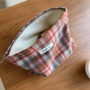 Detailed close-up of a red and blue plaid tweed toiletry bag with simple wish label