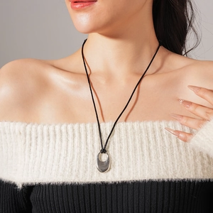Close-up of minimalist silver oval hollow pendant on a black cord worn by a model