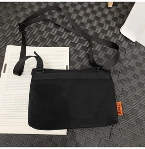 Detail of black crossbody bag featuring orange woven label and adjustable nylon strap
