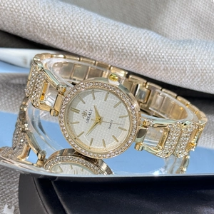 Détail de la montre à quartz dorée avec strass posée sur une surface miroir
