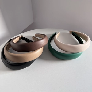 Set of four padded PU leather headbands in black, brown, beige, and green on a white table