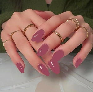 Gros plan d'ongles amande rose foncé avec des bagues dorées portées aux mains