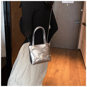 Silver metallic mini bag with 3D bow details and chain strap worn by a model