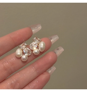 Close-up of golden zircon and freshwater pearl stud earrings held by hand