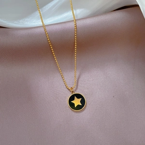 Détail d'un pendentif étoile dorée sur émail noir avec une fine chaîne à billes