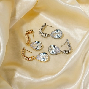 Elegant gold and silver pear-cut zircon teardrop earrings on a silk background