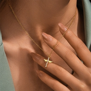 Detailed close-up of a gold angel wing cross pendant necklace with white zircons on a model