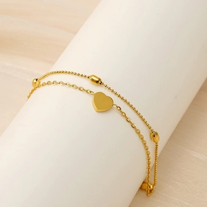 Detail of 18K gold double-layer anklet with heart charm on a white display stand
