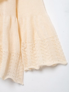 Detail of pointelle knit pattern and ruffled hem edge on a cream white knit sweater