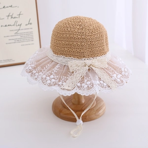 Detail of baby girl straw sun hat with white lace brim and decorative bow on wood stand