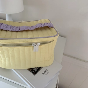 Detail of yellow quilted makeup bag with purple ruffled handle and zip closure