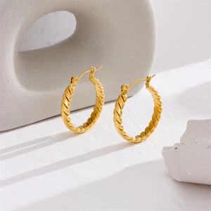 Minimalist thick gold twist hoop earrings in titanium steel on a modern geometric display