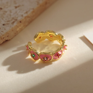 Detail of gold floral open ring with colorful gemstones and pink enamel petals