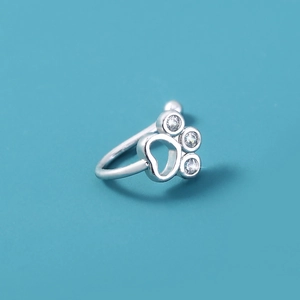 Macro detail of silver nose cuff with stone-encrusted paw print design on blue background
