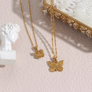 Detail of gold butterfly pendant necklaces on pink background with artistic plaster bust