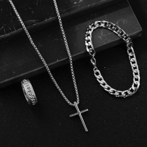 Close-up of silver steel set with cross necklace, curb bracelet and braided chain ring