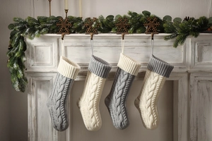 Close-up of four knitted Christmas stockings with cable patterns hanging on a fireplace