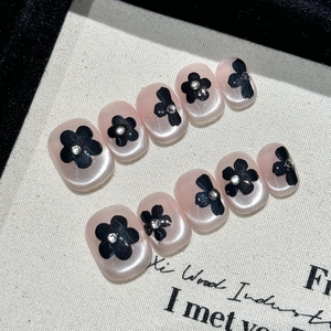 Handmade press-on nails with black floral patterns and bows on pink pearlescent base
