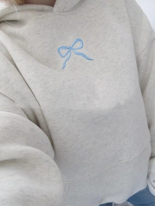 Detailaufnahme der blauen Schleifenstickerei auf einem grauen Baumwoll-Hoodie