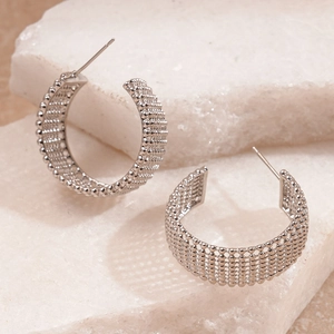 Detailed view of silver C-shaped metal hoop earrings with beaded woven texture on marble
