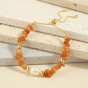 Detail of adjustable gold chain bracelet with orange stones and a large baroque pearl