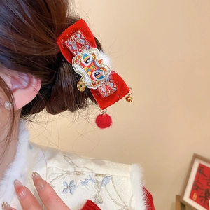 Detail of red velvet bow hair clip with lion dance embroidery and golden bell tassel