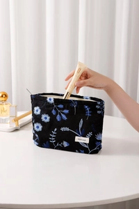 Detail view of a hand placing cosmetics into a black cotton bag with daisy embroidery