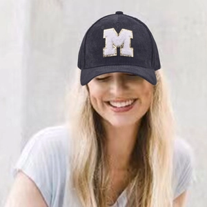 Detail of navy corduroy baseball cap featuring white M letter embroidery with gold trim