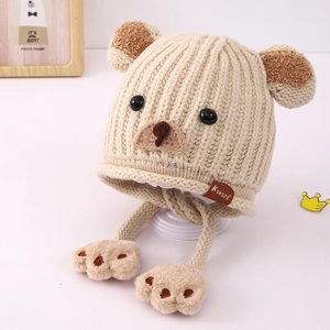 Detailansicht der beigen Bärenmütze mit Strickmuster, KUKUJI-Etikett und Plüsch-Pompons
