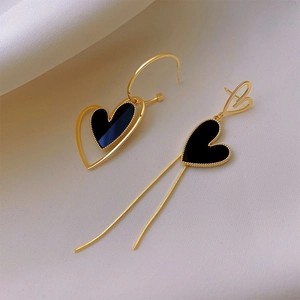Detailed shot of asymmetric gold heart earrings with black enamel and tassel fringe on silk