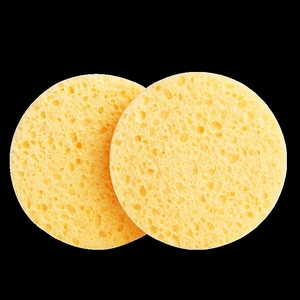 Two pieces of round yellow natural wood pulp sponges with porous texture on black background