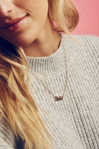 Close-up of golden Bella name pendant necklace on model with grey knit sweater